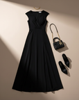 Flatlay of a black slit maxi dress paired with heels and a clutch displayed on a soft neutral surface.