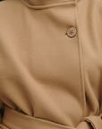 Nahaufnahme eines beigen Cape-Oberteils mit glatter Stoffstruktur, Knopfdetail und sauberer Verarbeitung.