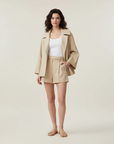 Frau trägt ein beigefarbenes Blazer- und Shorts-Set mit taillierter Passform und modernem, minimalistischem Stil.