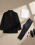 Schwarzer Blazer mit klassischem Revers und dezenter Struktur, flach ausgelegt neben Schuhen und Accessoires auf hellem Hintergrund.
