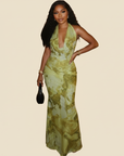 Model trägt ein grünes florales Maxikleid mit tiefem Ausschnitt und figurbetonter Form in einem minimalistischen Studio.