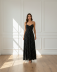 Model trägt ein gepunktetes schwarzes Maxikleid mit fließendem Schnitt in einem lichtdurchfluteten Innenraum.