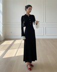 Model präsentiert ein elegantes schwarzes Maxikleid mit klassischer Linienführung und kontrastierenden Manschetten in einem minimalistischen Studio.