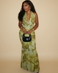 Model trägt ein grünes Maxikleid mit floralem Muster, tiefem Ausschnitt und eleganter Silhouette im warmen Studio.