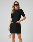 Model trägt ein schwarzes Minikleid mit kurzen Ärmeln, kontrastierendem Besatz und dezenter A-Linien-Silhouette im Studio.