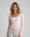 Model trägt ein rosa Wickeltop mit Wickeloptik, langen Ärmeln und femininer Passform im Studio.