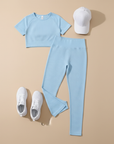 Hellblaues Crop-Top, Leggings und weiße Accessoires als Flatlay arrangiert.