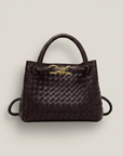 Dunkelbraune, geflochtene Handtasche mit goldener Metallschließe auf hellem Hintergrund, klar und hochwertig präsentiert.