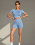 Frau trägt ein hellblaues kurzes Sportset mit figurbetonter Passform im Studio.