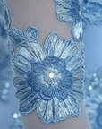 Nahaufnahme der blauen Blumenstickerei mit feiner Textur und dekorativen Blütenelementen auf transparentem Stoff.