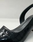 Nahaufnahme eines schwarzen Slingback-Schuhs mit strukturierter Oberfläche und mittlerem Absatz auf hellem Hintergrund.