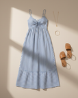 Blue striped sundress hanging on a wall with accessories placed beside it on a neutral background.