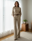 Woman wearing a beige knit long-sleeve top and matching wide-leg pants in soft natural indoor lighting.
