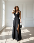 Woman wearing a black evening maxi dress with a thigh-high slit and fitted bodice in natural window lighting.