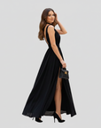 Woman wearing a black formal maxi dress with a high slit and sleeveless wrap design in a clean studio setting.