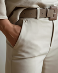 Close-up of beige trousers showing waistband, belt detail, pleats, and soft textured fabric.