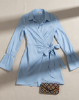 Flatlay of a blue wrap-style mini shirt dress showing front tie, long sleeves, and button-down collar.