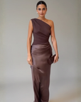 Model trägt ein braunes One-Shoulder-Abendkleid mit gerüschtem Detail und figurbetontem Schnitt im Studio.