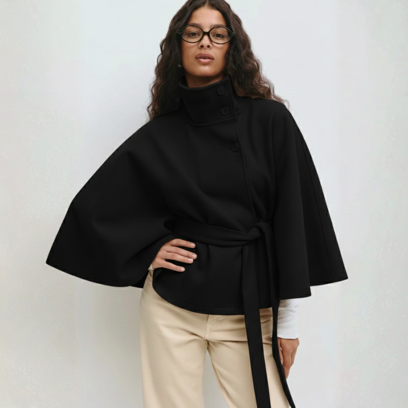 Model trägt ein schwarzes Cape-Oberteil mit weitem Schnitt und Bindegürtel, kombiniert mit heller Hose im Studio.