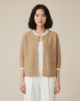 Beigefarbener Cardigan mit weißem Kontrastbesatz und goldenen Knöpfen, getragen von einem Model im Studio.