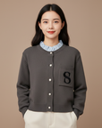 Model trägt einen grauen Cardigan mit Rundhalsausschnitt, Knopfleiste und gesticktem „S“-Detail vor neutralem Hintergrund.
