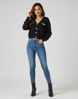 Model trägt einen schwarzen Cardigan mit weißem Kontrastbesatz und goldenen Knöpfen, kombiniert mit Jeans für einen modernen Look.
