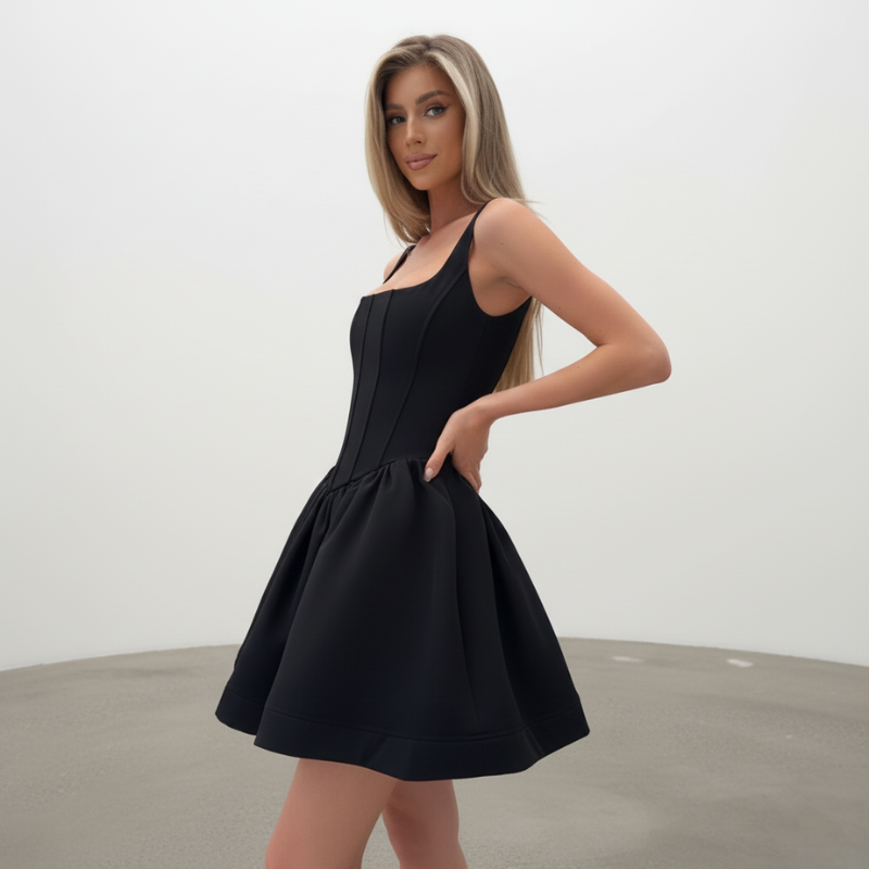 Model trägt ein schwarzes Kleid mit ausgestelltem Ballonrock und klarer Silhouette in einem sonnigen Innenraum.
