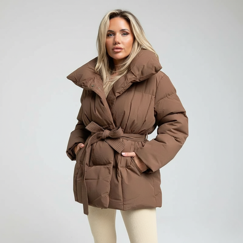 Model präsentiert eine braune Daunenjacke mit Gürtel und klarer Linienführung im Studio.