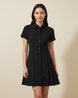 Model trägt ein schwarzes kurzes Hemdblusenkleid mit Knopfleiste, klassischem Kragen und ausgestellter Silhouette im Studio.