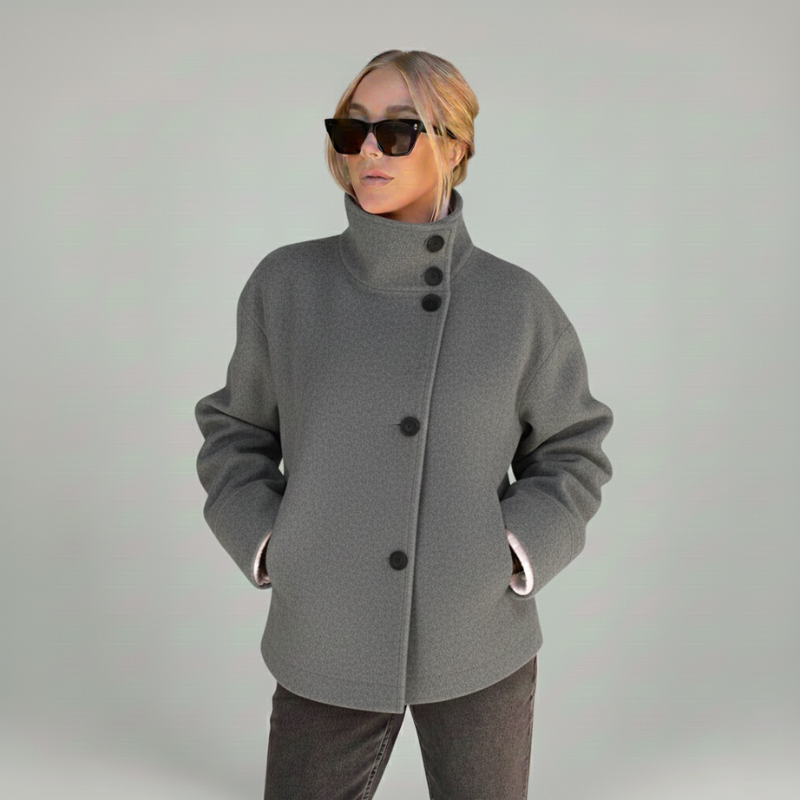 Graue Wolljacke mit breitem Kragen, seitlichen Taschen und moderner Silhouette, getragen in einer klaren Outdoor-Studioaufnahme.