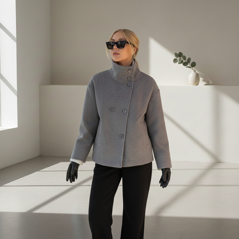Model trägt eine graue Wolljacke mit lockerer Passform und modernem Schnitt in einem minimalistischen Innenraum.