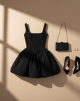 Schwarzes Minikleid mit breiten Trägern und Ballonrock flach ausgelegt auf hellem Hintergrund, ergänzt durch Accessoires.