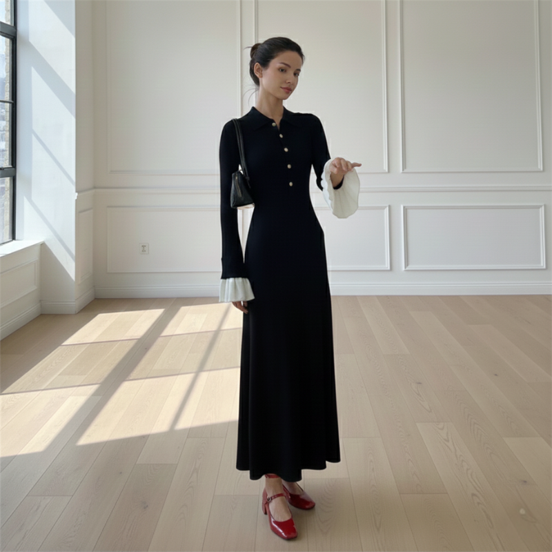 Model präsentiert ein elegantes schwarzes Maxikleid mit klassischer Linienführung und kontrastierenden Manschetten in einem minimalistischen Studio.
