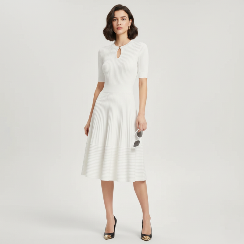 Model trägt ein weißes plissiertes Kleid mit kurzem Ärmel, goldenen Knöpfen und ausgestelltem Rock in heller Umgebung.