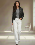 Model trägt eine schwarze Lederjacke kombiniert mit weißer Stoffhose und hellem Oberteil in einem lichtdurchfluteten Studio.