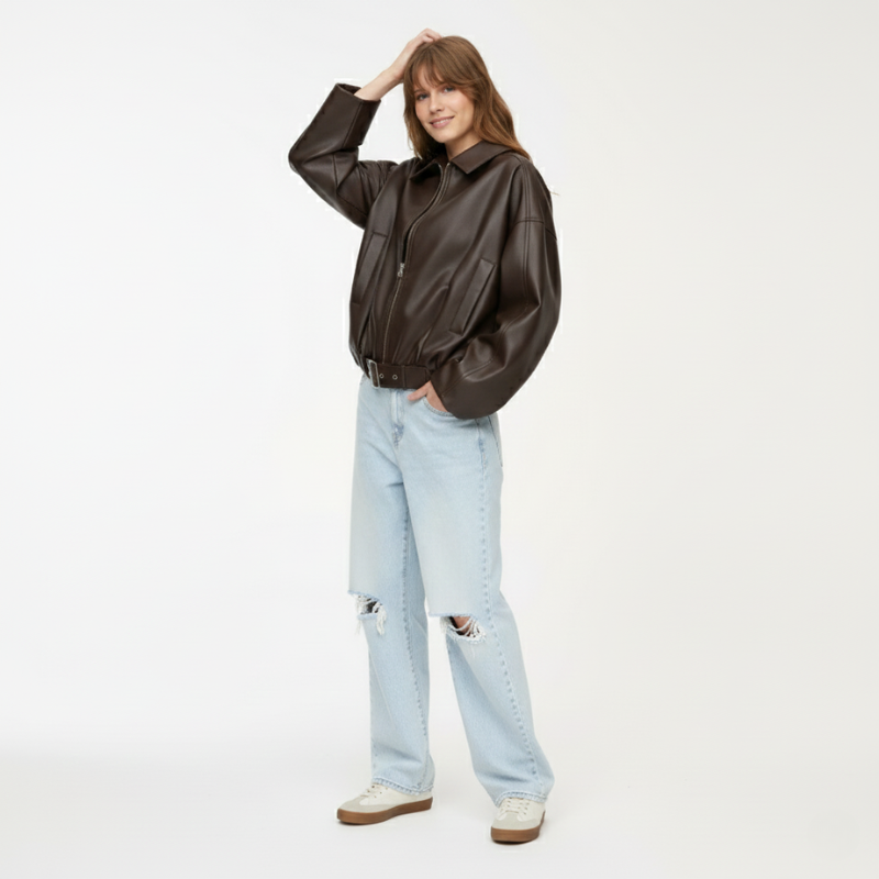 Frau posiert in schwarzer Lederjacke und Jeans in einer natürlichen, lässigen Studioaufnahme.