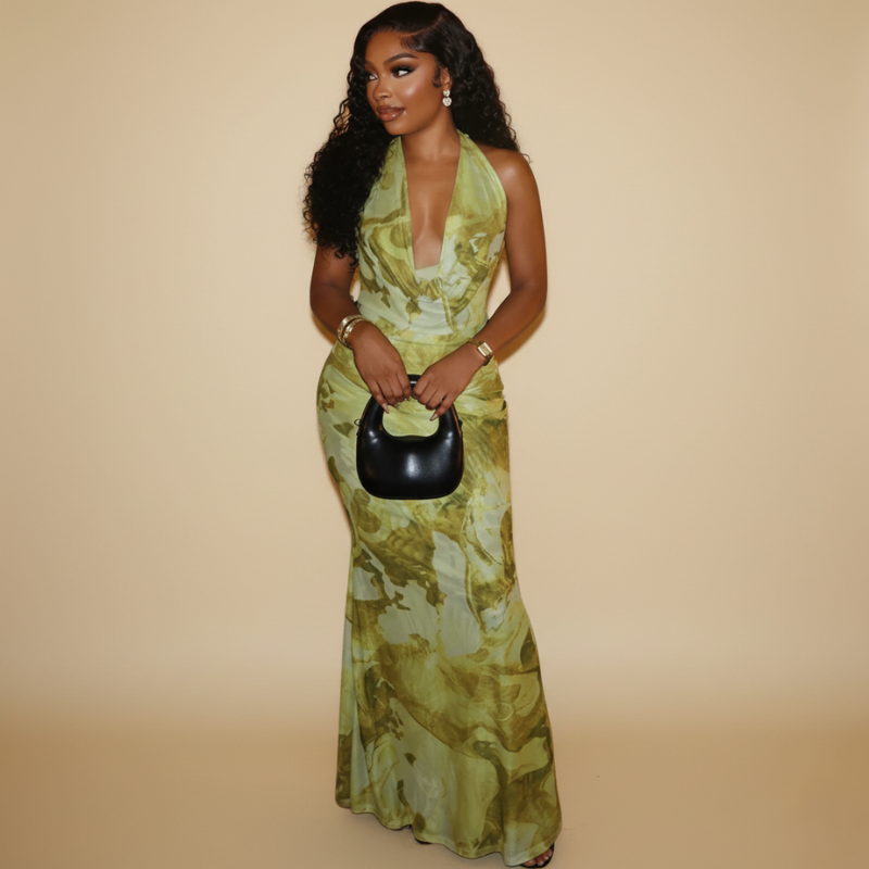 Model trägt ein grünes Maxikleid mit floralem Muster, tiefem Ausschnitt und eleganter Silhouette im warmen Studio.