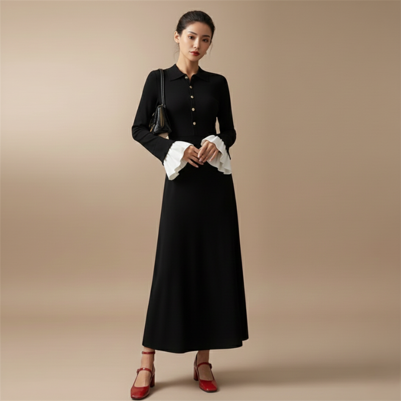 Model trägt ein schwarzes Maxikleid mit goldenen Knöpfen, strukturiertem Oberteil und kontrastierenden weißen Manschetten im Studio.