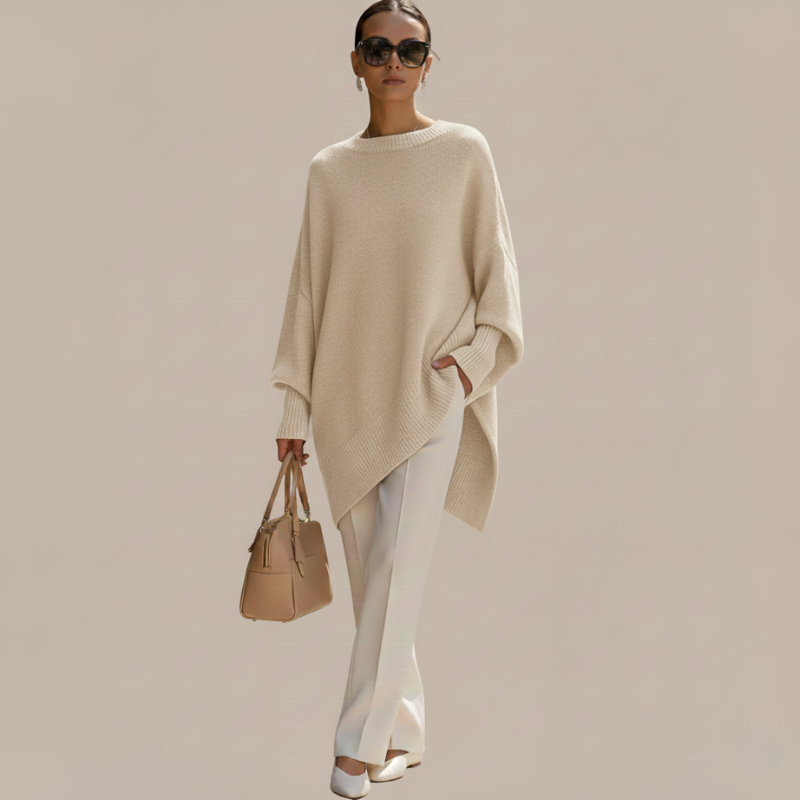 Model geht in einem beigen Oberteil mit fließendem Schnitt und heller Hose vor neutralem Hintergrund.