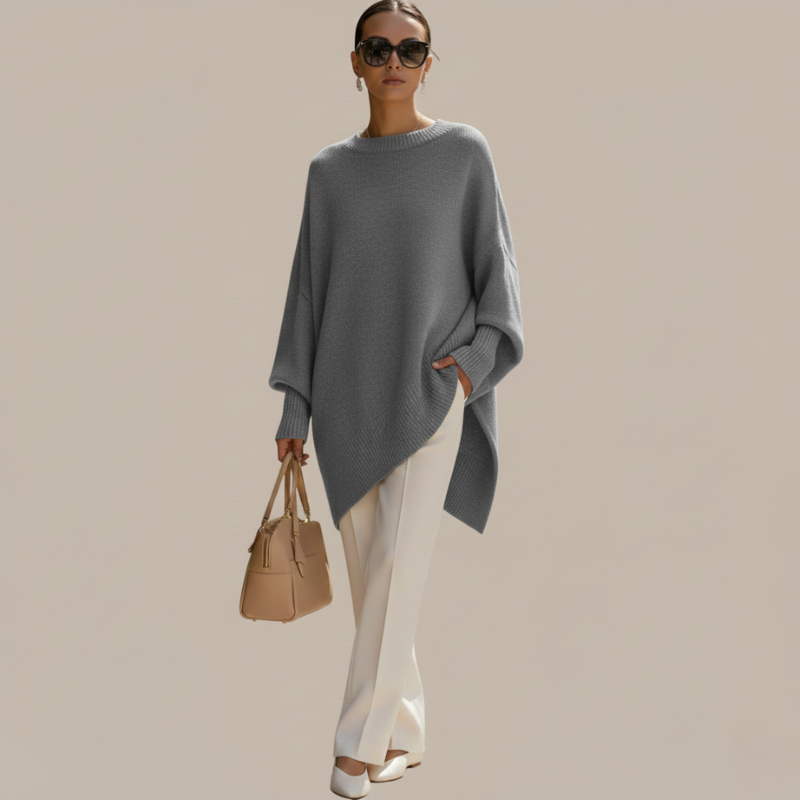 Frau trägt ein graues Oberteil mit fließendem Schnitt, kombiniert mit weißer Hose im neutralen Studio.