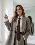 Model trägt einen braun karierten Oversize-Blazer mit weißem Hemd und Krawatte im hellen Studio für einen modernen Business-Look.