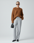 Model trägt einen braunen Oversize-Pullover mit weicher Strickstruktur und weiter Silhouette, kombiniert mit grauer Hose im Studio.