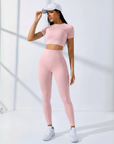 Modell trägt ein rosa Sport-Set mit Crop-Top und Leggings in heller Umgebung.