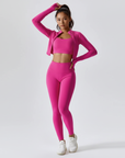 Model trägt ein pinkfarbenes zweiteiliges Sportset mit Crop-Top und hoch taillierter Leggings in klarer Studioaufnahme.