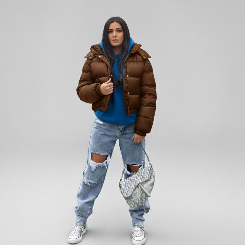 Frau präsentiert eine blaue Steppjacke mit Kapuze, kombiniert mit weiter Jeans im neutralen Studio.