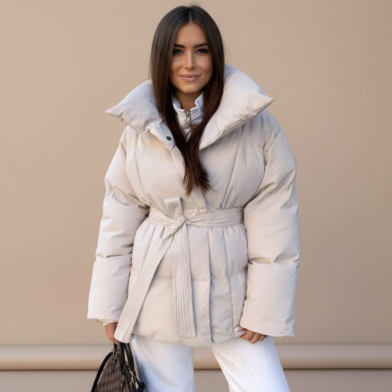 Model trägt eine cremefarbene Steppjacke mit Bindegürtel, hohem Kragen und strukturierter Silhouette im Studio.