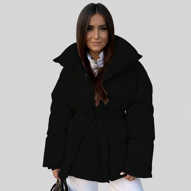 Frau präsentiert eine schwarze Steppjacke mit Kapuze und geradem Schnitt vor neutralem Hintergrund.