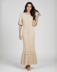 Model trägt ein langes beiges Strickkleid mit ärmellosem Design, dezenter Struktur und eleganter Passform im Studio.