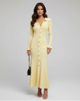 Model trägt ein langes gelbes Strickkleid mit Knopfleiste und eleganter Silhouette in einem minimalistischen Studio.
