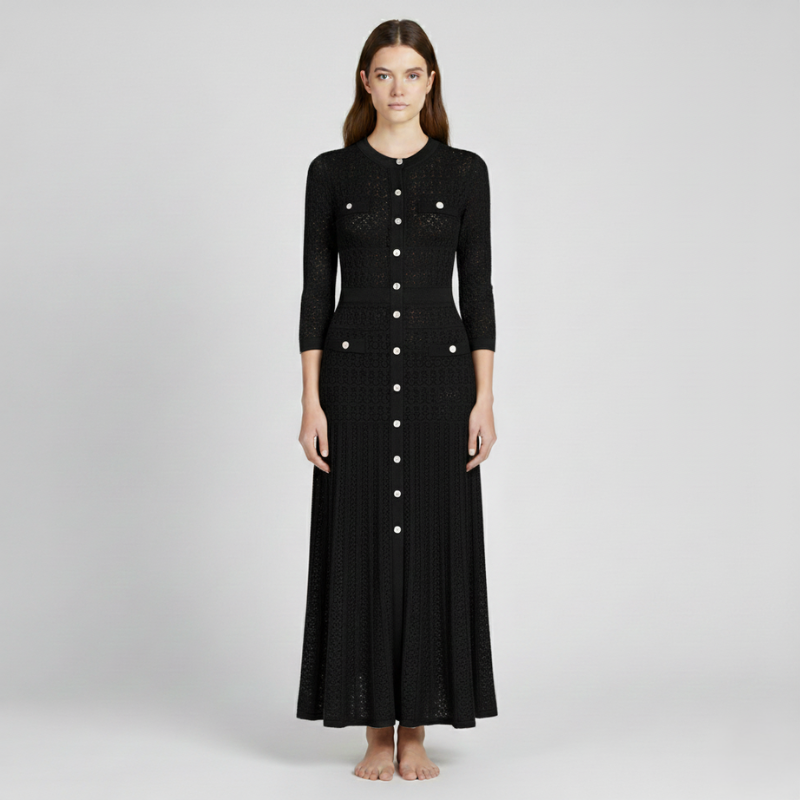 Model trägt ein schwarzes langes Strickkleid mit dekorativem Lochmuster und schlichter Silhouette im neutralen Studio.*